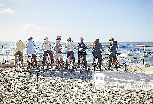 Active senior tourist friends on bicycles looking at sunny ocean view
