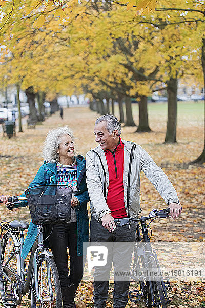 Älteres Paar  das zwischen Bäumen und Blättern im Herbstpark Fahrrad fährt