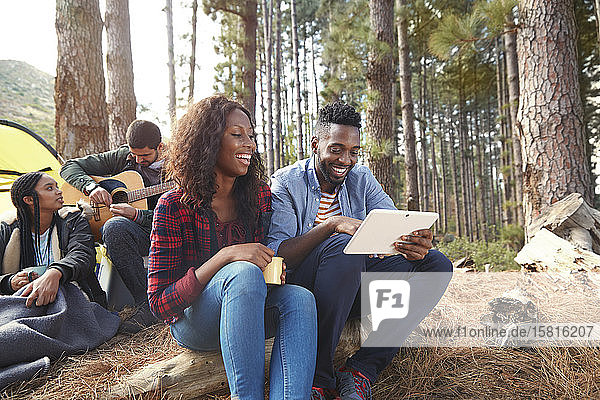 Lächelndes junges Paar  das auf einem Campingplatz im Wald ein digitales Tablet benutzt