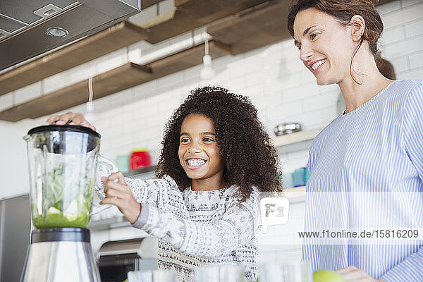 Mutter und Tochter machen einen gesunden grünen Smoothie im Mixer in der Küche