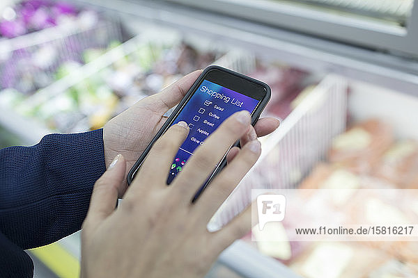 Nahaufnahme einer Frau  die mit ihrem Smartphone im Supermarkt eine Einkaufsliste erstellt
