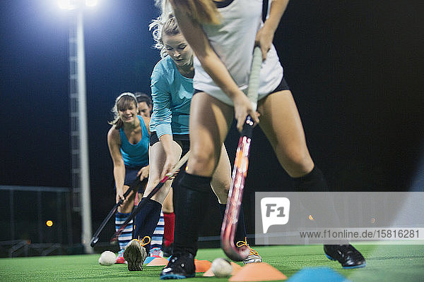 Entschlossene junge Feldhockeyspielerinnen üben nachts auf einem Feld eine Sportübung