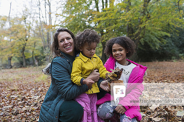 Portrait happy mother and daughters playing in autumn leaves in woods