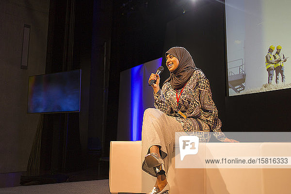 Lächelnde Sprecherin mit Mikrofon im Hidschab auf der Bühne