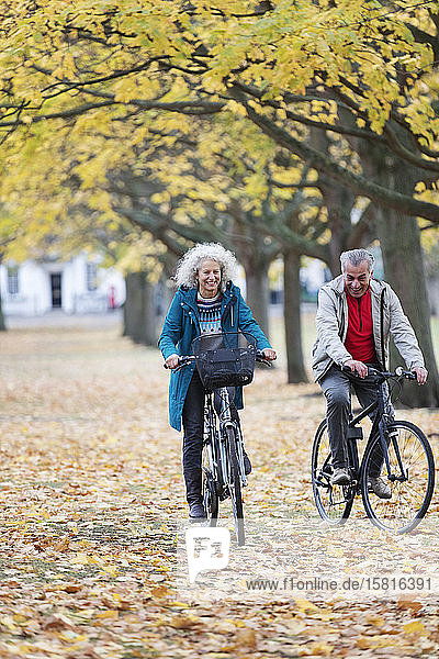 Älteres Paar fährt mit dem Fahrrad zwischen Blättern und Bäumen im herbstlichen Park