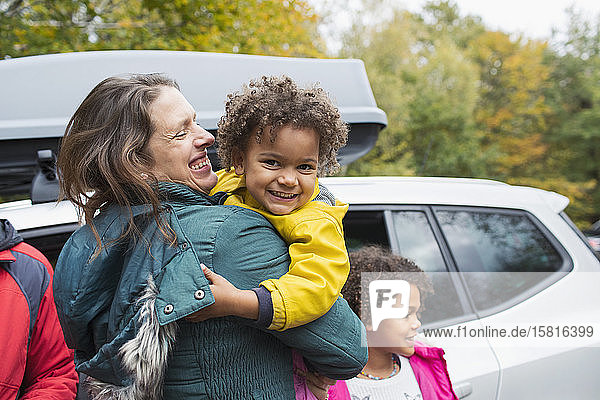 Porträt einer glücklichen Mutter  die ihre Tochter vor einem Auto auf einem Parkplatz hält