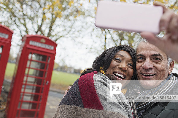 Zärtliches älteres Paar macht ein Selfie im Herbstpark vor einem roten Telefonbuch