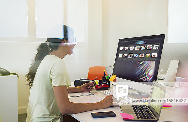 Weibliche Designerin betrachtet Bildminiaturen am Computer im Büro