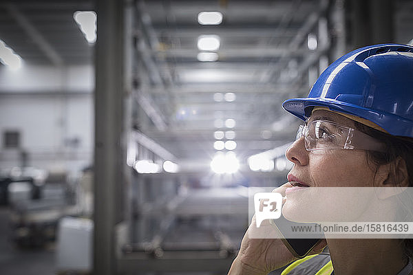 Weiblicher Arbeiter  der in einer Fabrik mit einem Handy telefoniert