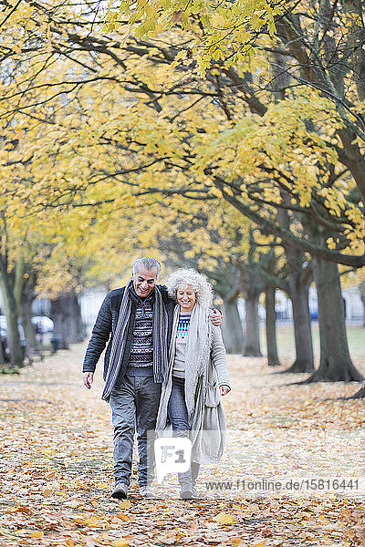 Zärtliches älteres Paar  das zwischen Bäumen und Blättern im Herbstpark spazieren geht