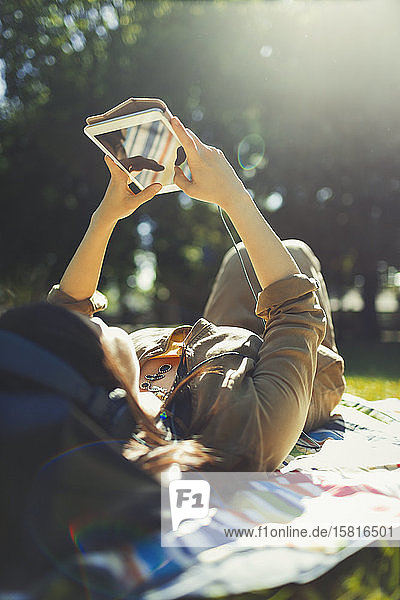 Junge Frau entspannt sich und benutzt ein digitales Tablet in einem sonnigen Sommerpark