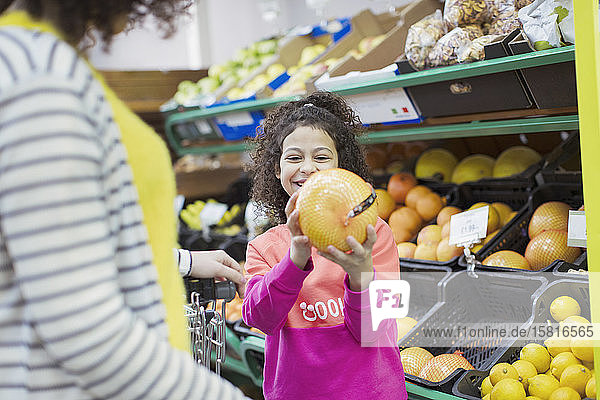 Lächelnde Tochter zeigt der Mutter im Supermarkt eine Grapefruit