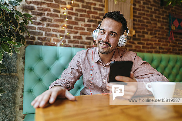 Lächelnder Mann in einem Café  der mit Kopfhörern Musik hört