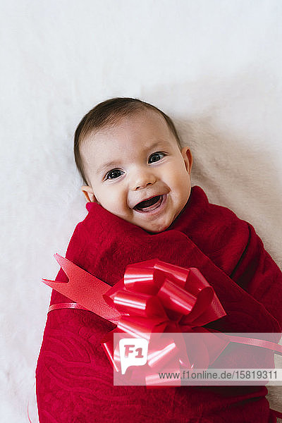 Porträt eines glücklichen Mädchens als Weihnachtsgeschenk verpackt mit roter Schleife auf weißem Hintergrund