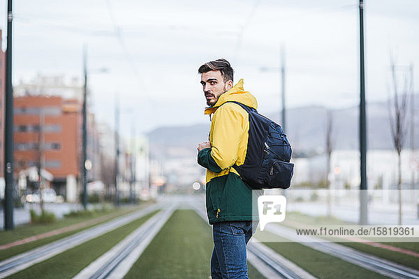 Porträt eines Mannes mit Rucksack in der Stadt auf Straßenbahnschienen