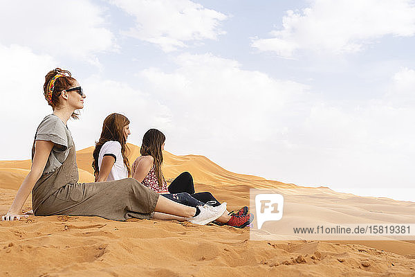 Drei junge Frauen sitzen in einer Sanddüne in der Wüste Sahara  Merzouga  Marokko
