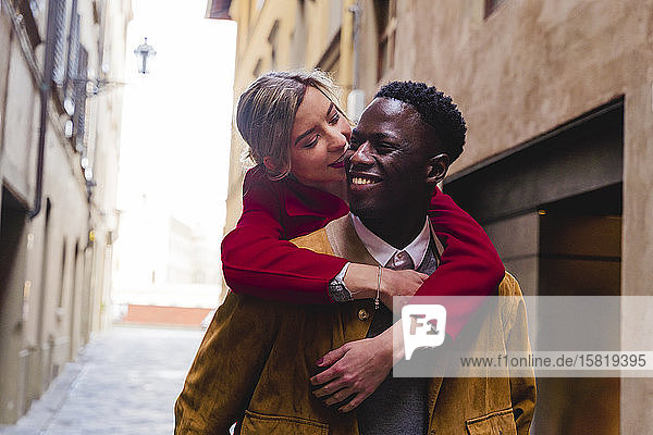 Happy young man carrying girlfriend piggyback in an alley in the city of Florence  Italy