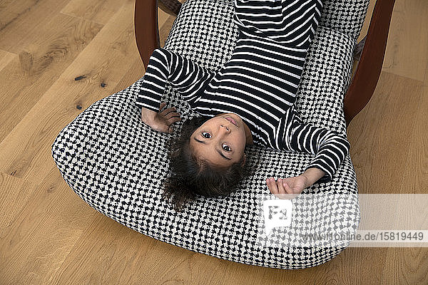 Portrait of little girl lying upside on armchair