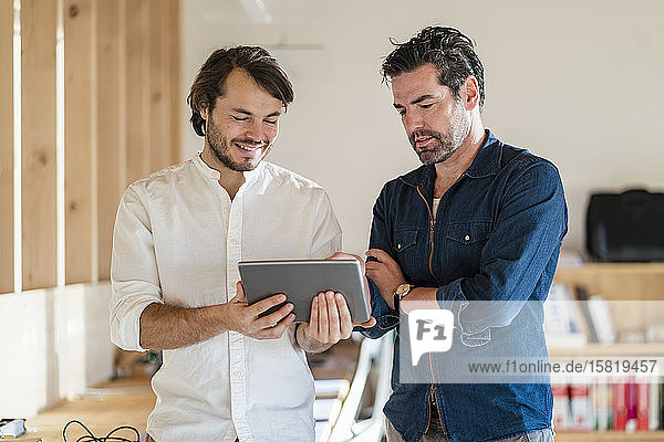 Two businessmen with tablet talking in wooden open-plan office