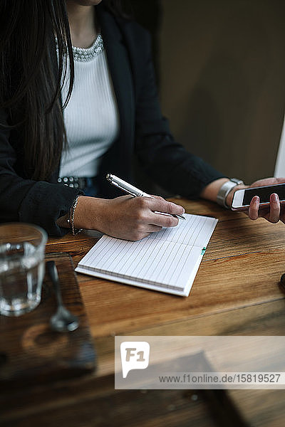 Scherenschnittansicht einer Frau mit Smartphone in einem Café  die Notizen macht