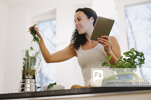 Fitte Frau steht in der Küche  bereitet gesunden Smoothie zu  mit Online-Rezept