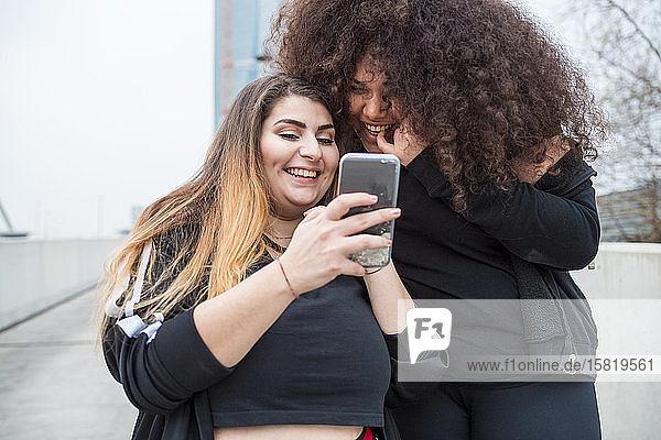 Zwei glückliche  sportliche junge Frauen  die in der Stadt ein Smartphone benutzen