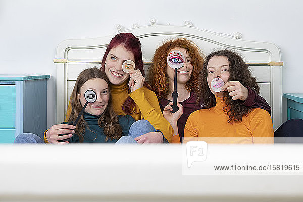 Family portrait of mother and her three daughters sitting together on bed holding paper masks