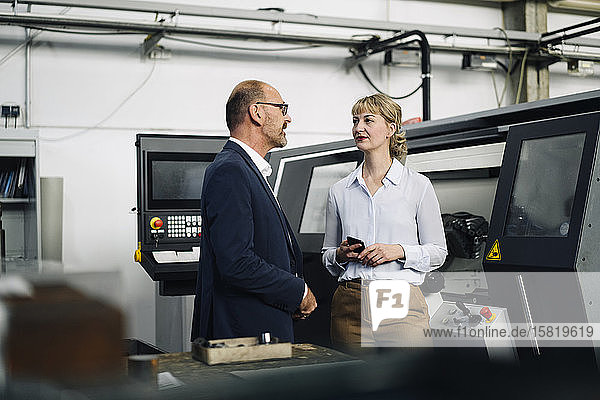 Businessman and woman with cell phone talking in a factory
