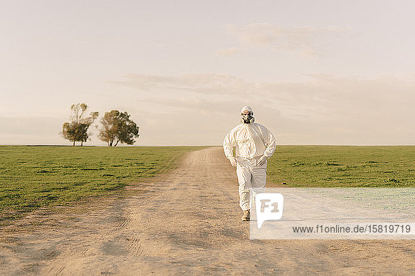 Mann mit Schutzanzug und Maske läuft auf Feldwegen auf dem Land