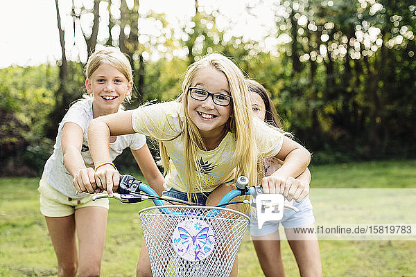 Glückliche Mädchen fahren Fahrrad im Garten