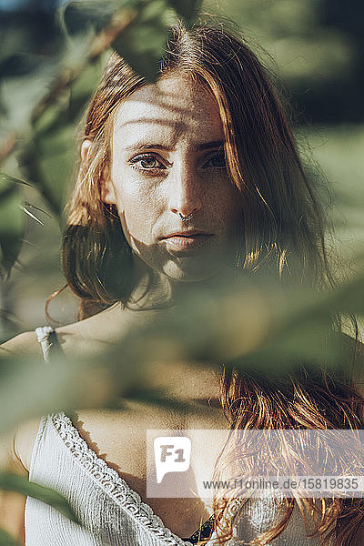Porträt einer rothaarigen Frau mit Nasenpiercing zwischen Zweigen  die in die Kamera schaut