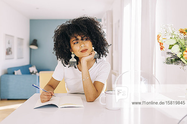 Portrait of young woman with curly hair sitting at a table with a notebook at home