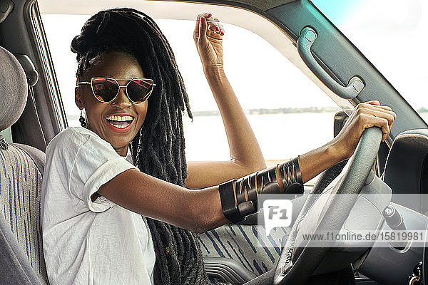 Porträt einer lachenden Frau mit Dreadlocks beim Autofahren
