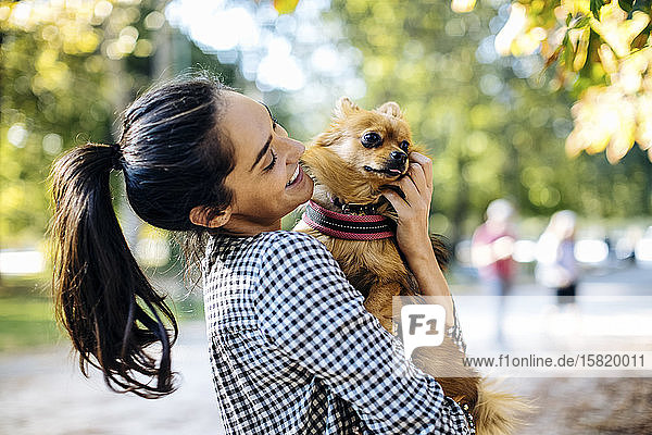 Happy young woman holding dog in a park