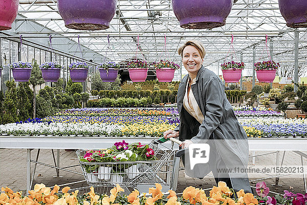 Smiling woman with pansies in shopping cart in flower shop