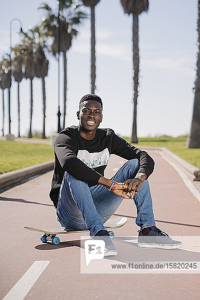 Porträt eines lächelnden jungen Mannes auf einem Skateboard sitzend