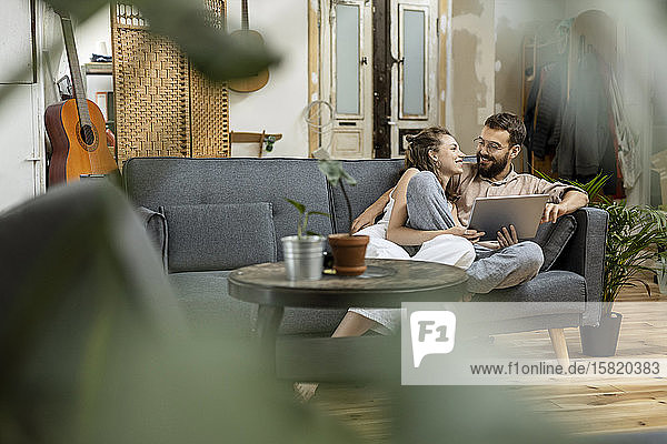Junges Paar sitzt zu Hause auf dem Sofa und benutzt ein digitales Tablett