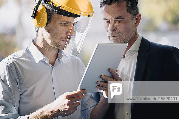 Businessman and man wearing safety helmet looking at tablet