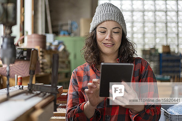 Porträt einer lächelnden Handwerkerin  die in ihrer Werkstatt Tabletten benutzt