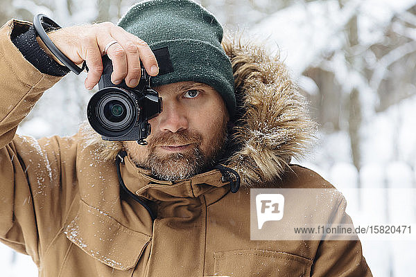 Portrait of bearded man taking photo of viewer with digital camera in winter