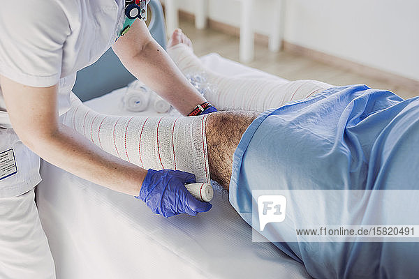 Krankenschwester wickelt im Krankenhausbett einen Verband um das Bein des Patienten