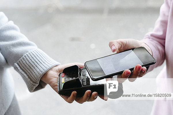 Hand einer Frau  die mit ihrem Smartphone bargeldlos am POS-Terminal bezahlt