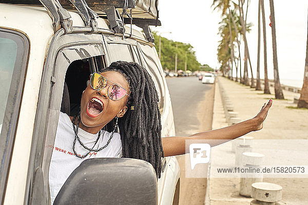 Porträt einer schreienden Frau mit Dreadlocks  die sich aus dem Autofenster lehnt  Maputo  Mosambik