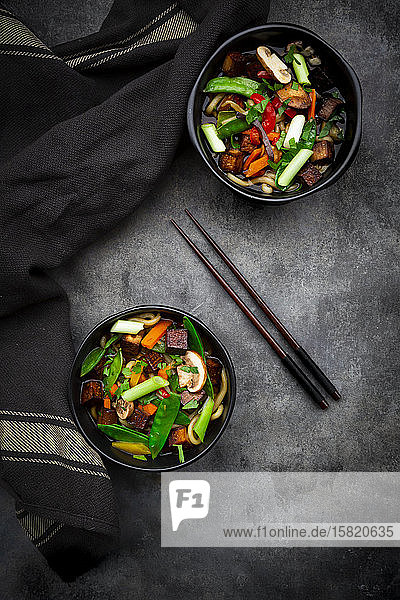 Zwei Schüsseln verzehrfertige Misosuppe mit Udon-Nudeln Tofu Zuckererbsen Paprika Karotten Mu-err-Pilzen Schalotten und Koriander