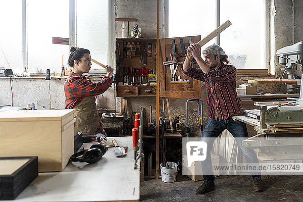 Verspielte Handwerkerin und Handwerker kämpfen in ihrer Werkstatt