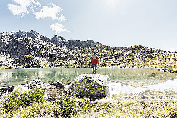 Rückansicht eines jungen Mannes auf einem Felsen mit Blick auf einen klaren Bergsee