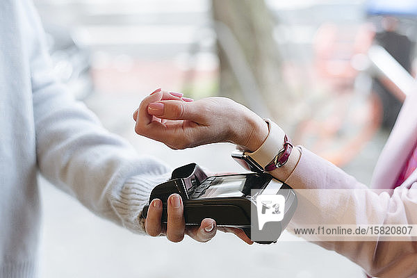 Hand einer Frau  die mit ihrer Smartwatch bargeldlos am POS-Terminal bezahlt