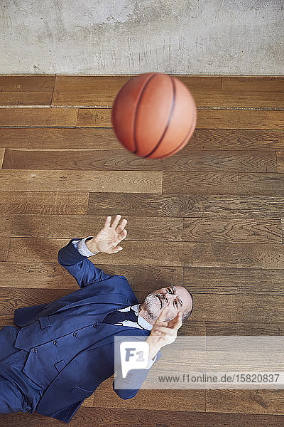 Leitender Geschäftsmann auf Holzboden liegend  mit Basketball spielend