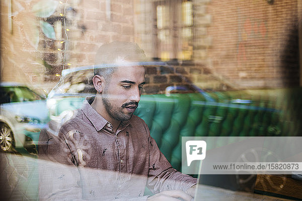 Mann hinter einer Fensterscheibe in einem Café mit Laptop