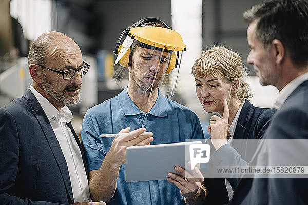 Geschäftsleute und Arbeiter mit Tabletten im Gespräch in einer Fabrik
